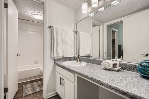 A bathroom with a white sink and a white towel hanging on the shower rod.