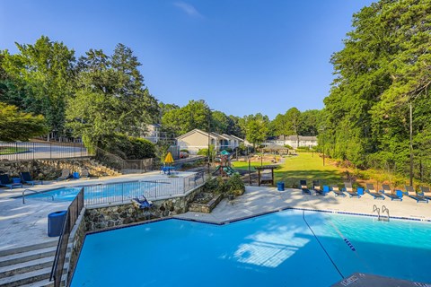 A large outdoor swimming pool surrounded by trees and a grassy area.