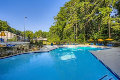 A large blue swimming pool surrounded by trees and a stone wall.