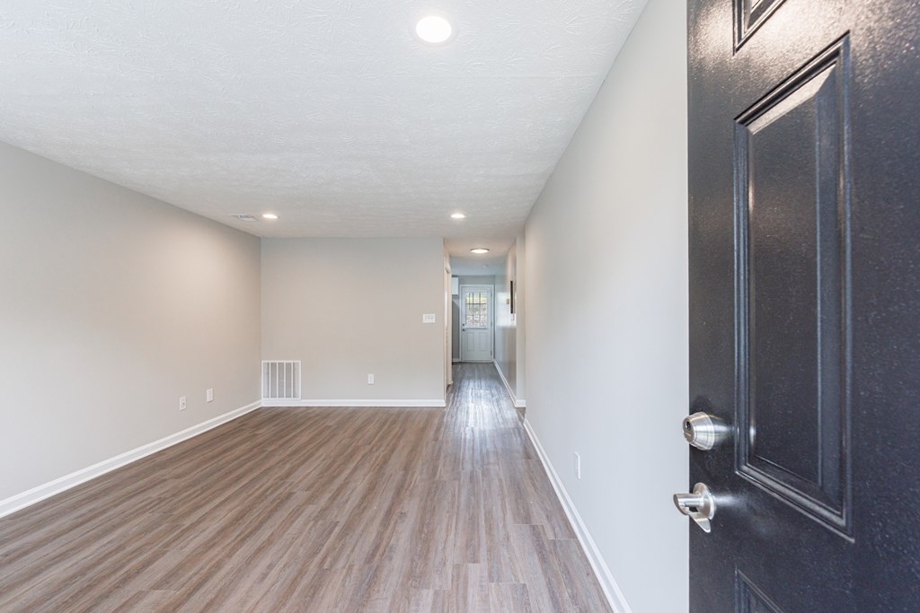 A hallway with a black door and wooden floors.