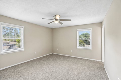 A room with a ceiling fan and two windows.
