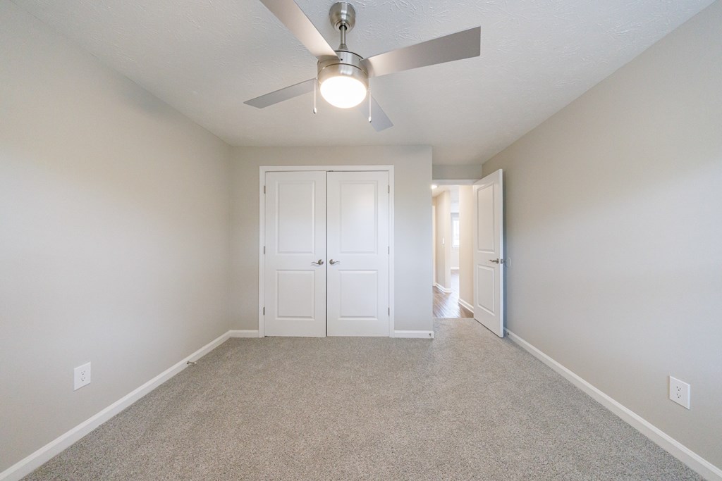 A room with a ceiling fan and carpeted floor.