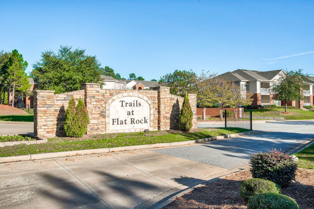 A sign that says Trails at Flat Rock stands in front of a gated entrance.