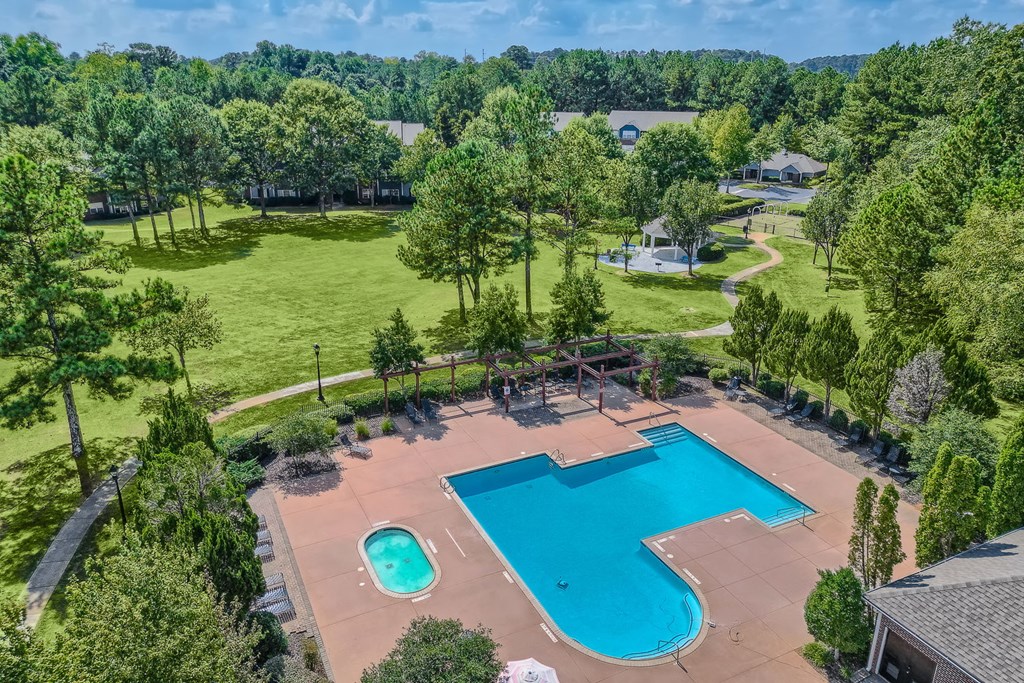 an aerial view of a swimming pool with trees and a park in the background