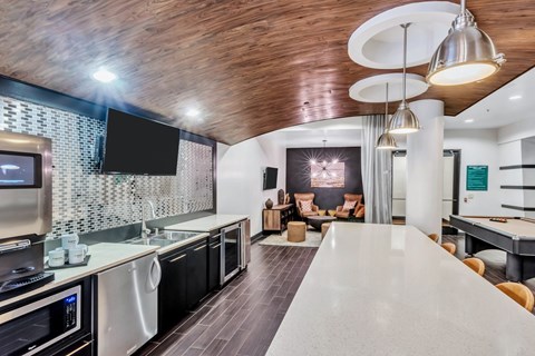 A modern kitchen with a long white counter top and a wooden ceiling.