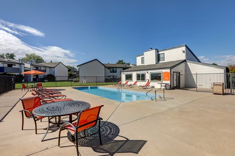 A pool with chairs and a table in front of a house.