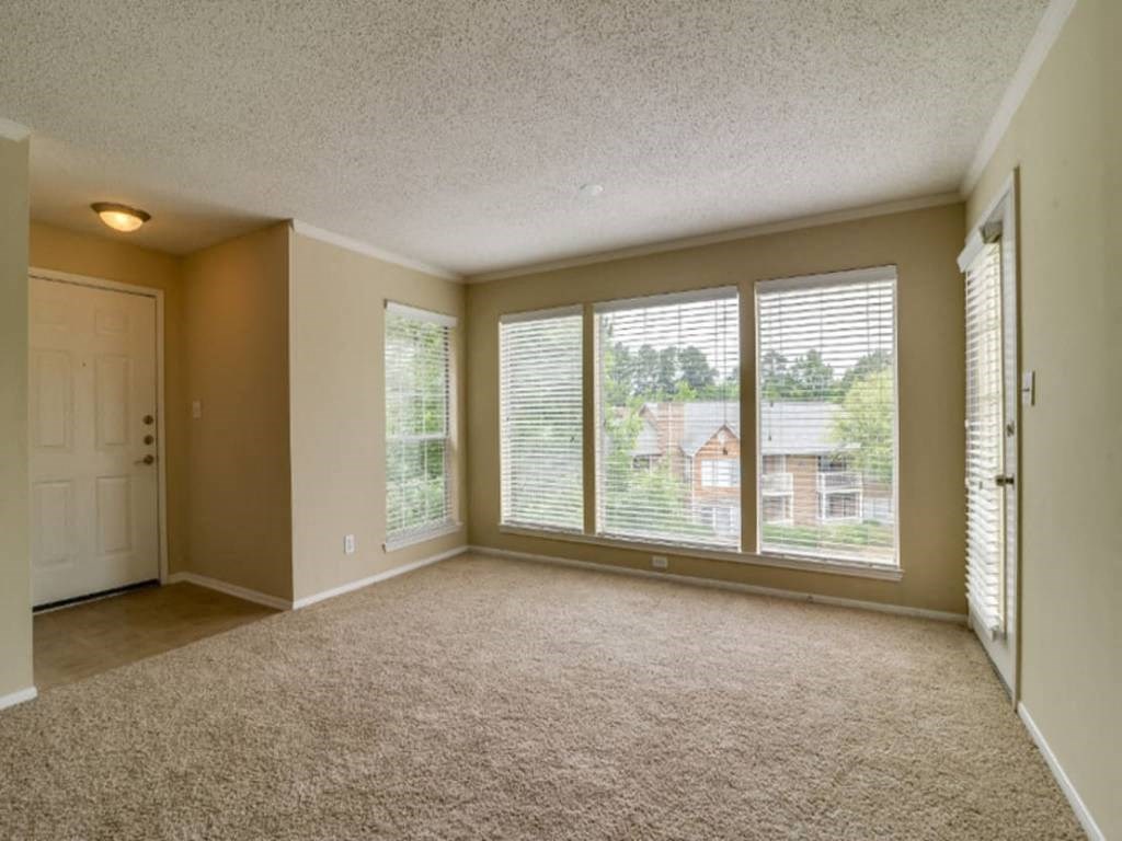 an empty living room with large windows and carpeting