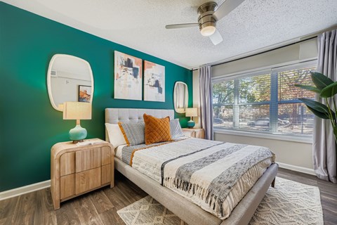 A bedroom with a bed, nightstand, and a window with a view of a building outside.