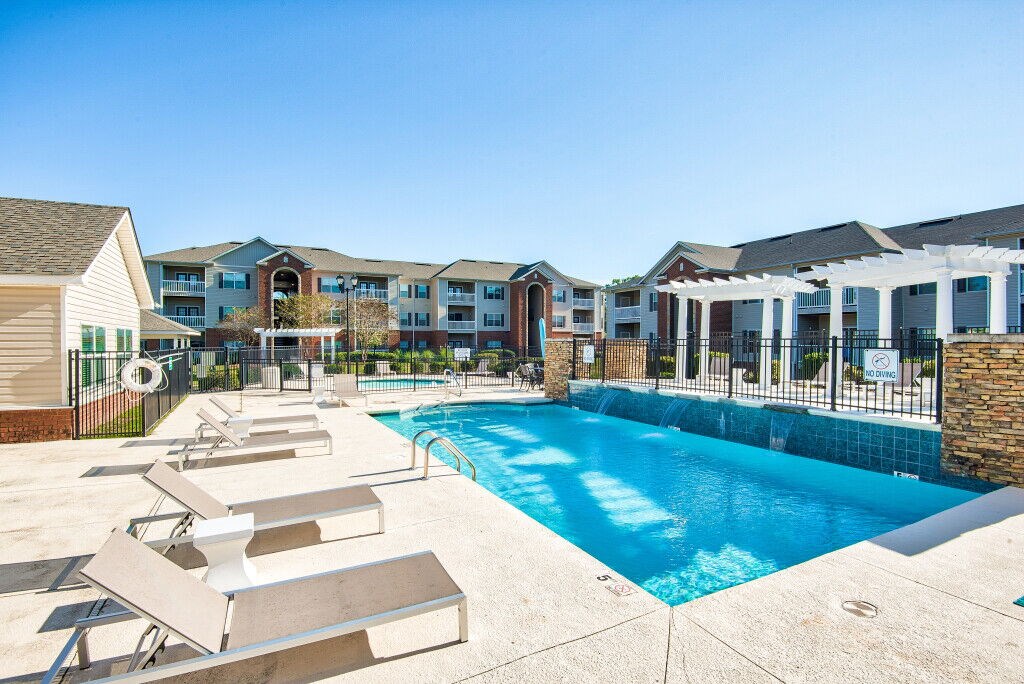 A swimming pool surrounded by sun loungers and apartment buildings.
