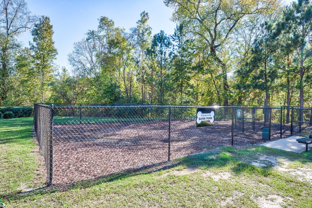 A chain link fence surrounds a grassy area with trees in the background.