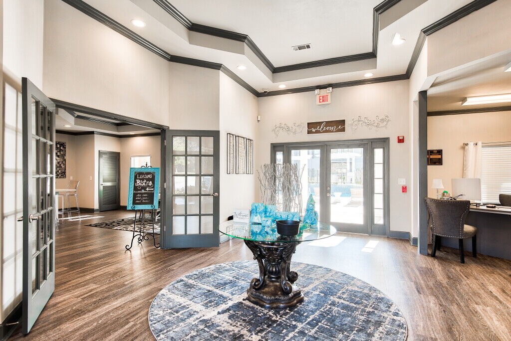 A foyer with a large rug and a vase of flowers.