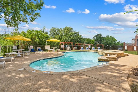 A large outdoor swimming pool surrounded by a concrete patio and a fence.