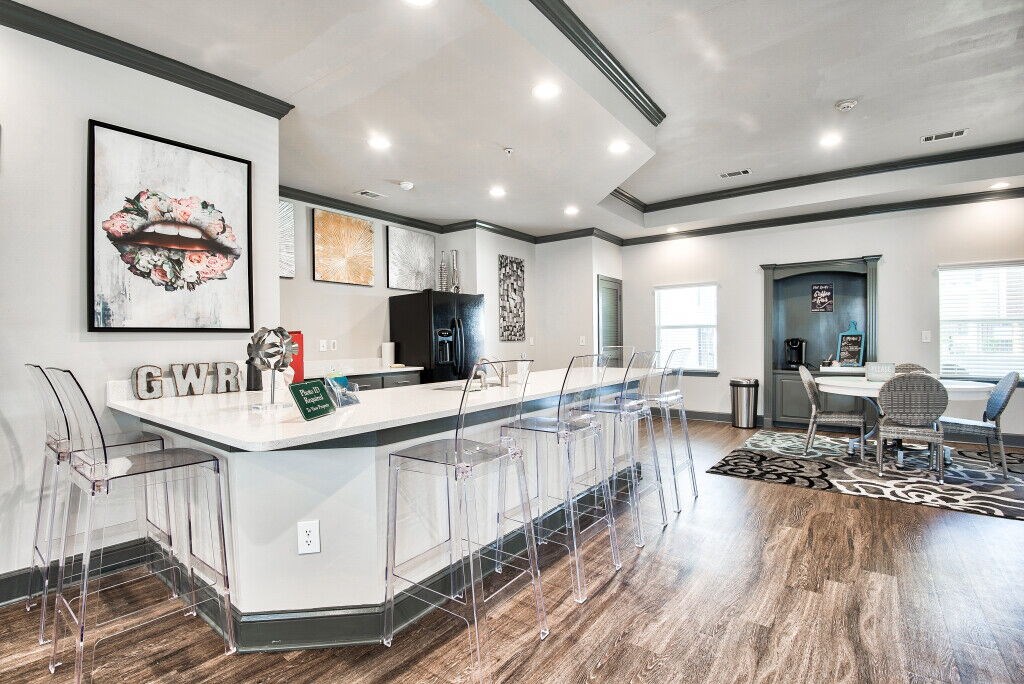 A modern kitchen with a white island and clear chairs.