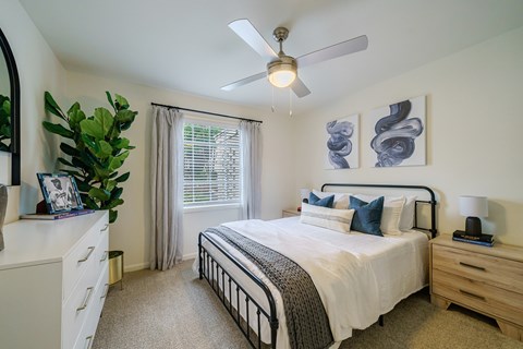 A bedroom with a bed, nightstand, and a plant.