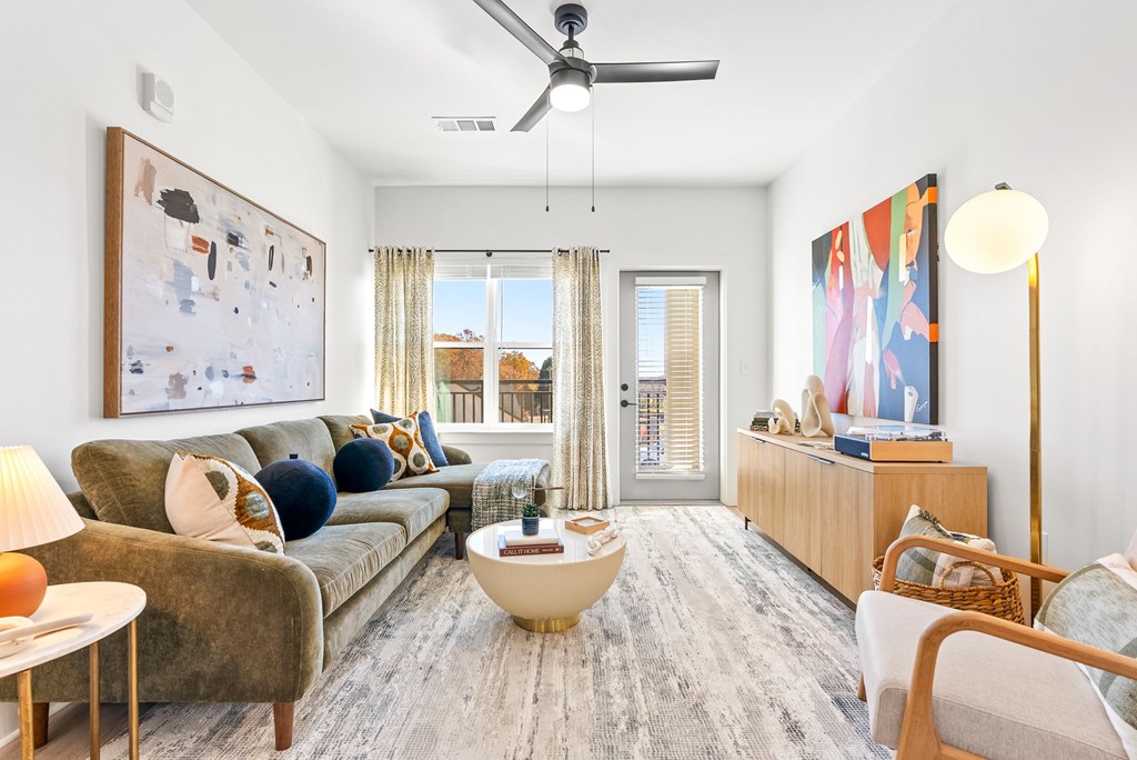 A living room with a grey couch, a coffee table, a ceiling fan, and a painting on the wall.