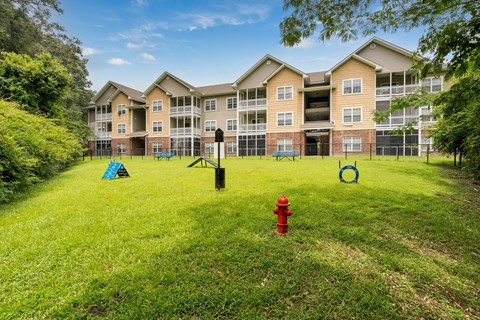 A red fire hydrant sits in the middle of a grassy area in front of apartment buildings.