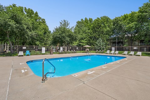A large blue swimming pool surrounded by trees and chairs.
