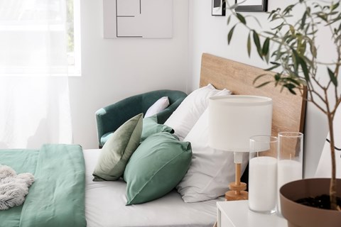 A cozy bedroom scene with a bed, a lamp, and a potted plant.