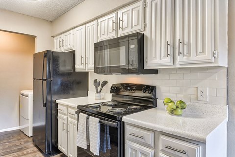 A black refrigerator is in a kitchen with white cabinets.