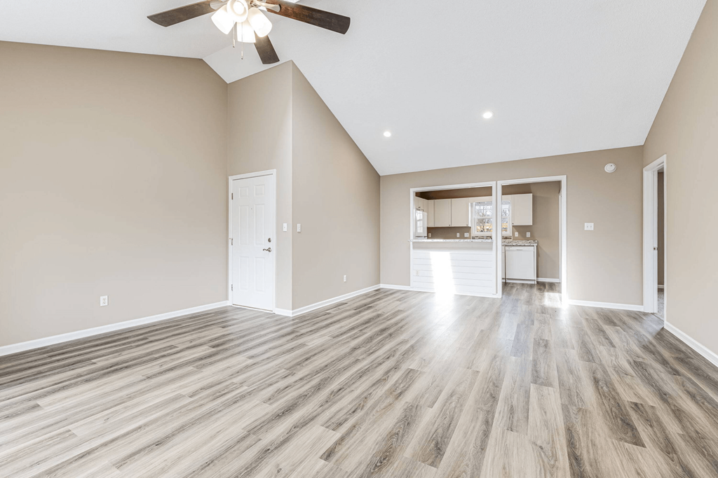 an empty living room with a ceiling fan and a kitchen