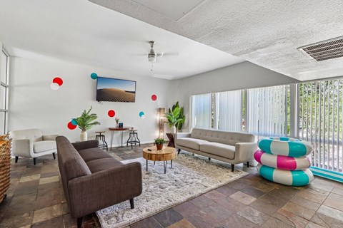 A living room with a brown couch, a white chair, a white sofa, a white rug, a brown coffee table, a white ceiling fan, a white wall, a white door, a white window, a white curtain,