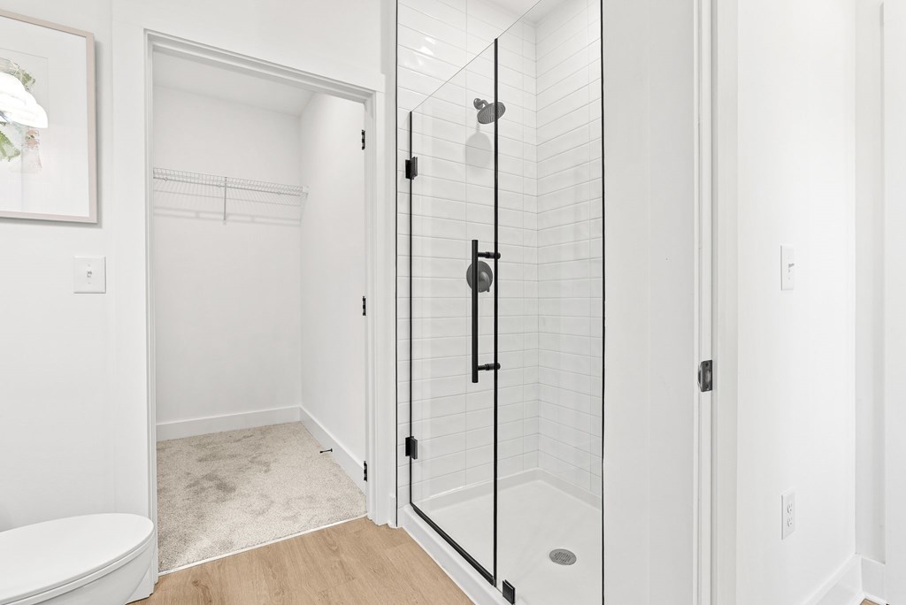 A white bathroom with a toilet, a walk in shower, and a towel rack.