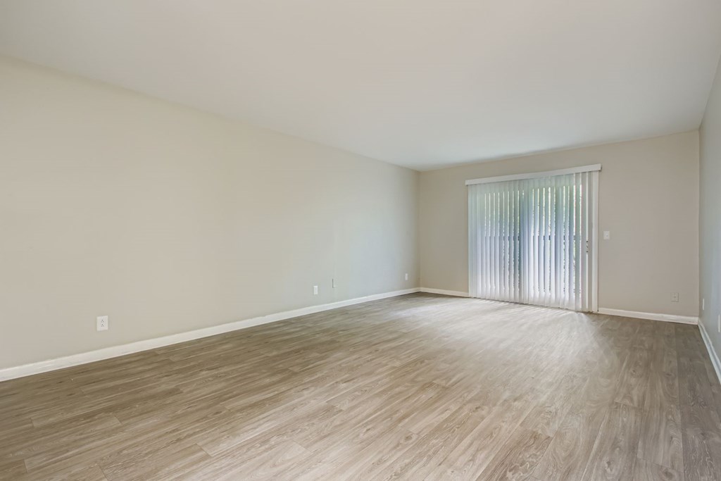 Empty room with wooden flooring and a window with blinds.