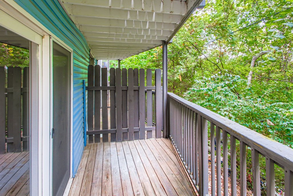 A wooden deck with a railing and a view of a green forest.