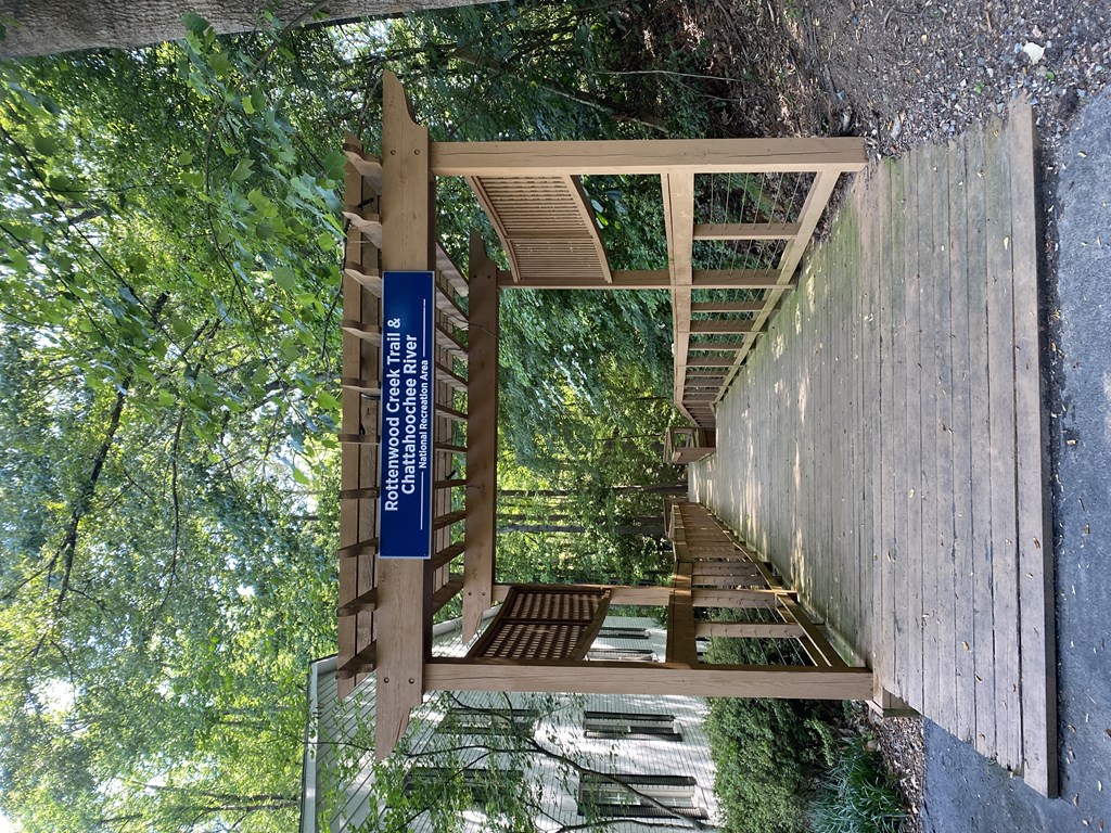 a walkway in a forest with a blue sign on the side of the walkway at Vinings RiverVue Apartments, Georgia