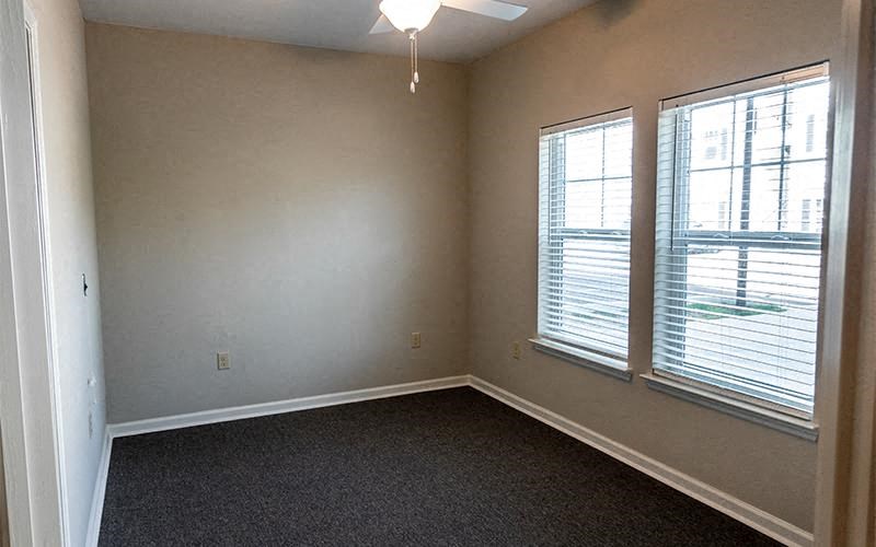 an empty room with two windows and a ceiling fan