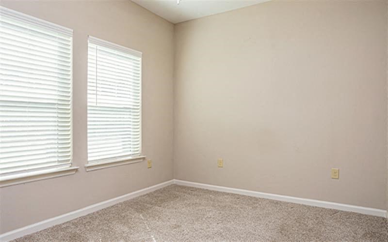 an empty room with two windows and a carpet