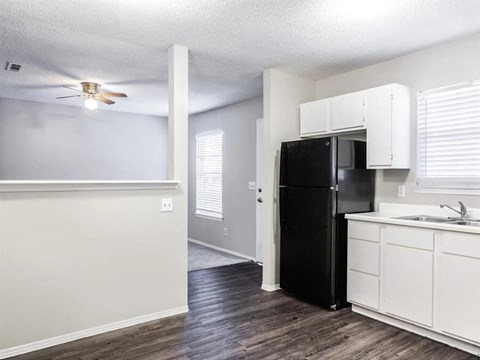 A black refrigerator is in a kitchen with white cabinets.