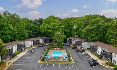 A view of a parking lot with a swimming pool and trees in the background.