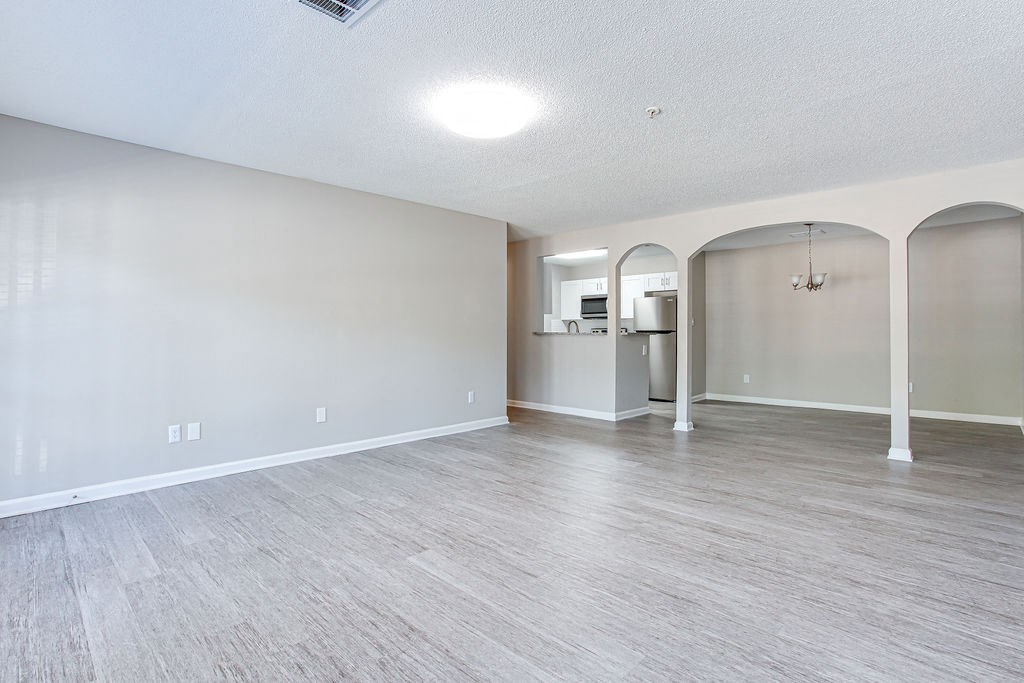 an empty living room with a kitchen in the background