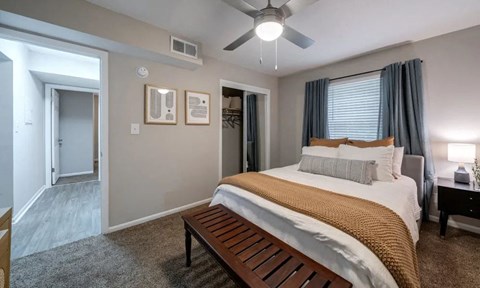 A bedroom with a bed, a bench, and a ceiling fan.