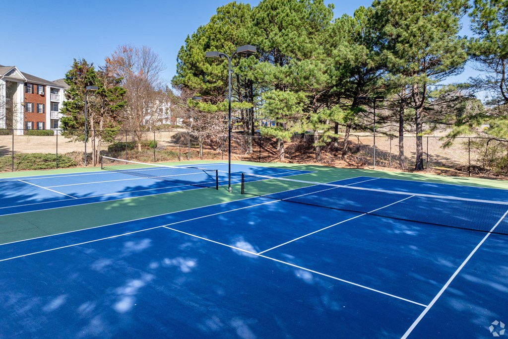 two tennis courts with trees in the background on a sunny day