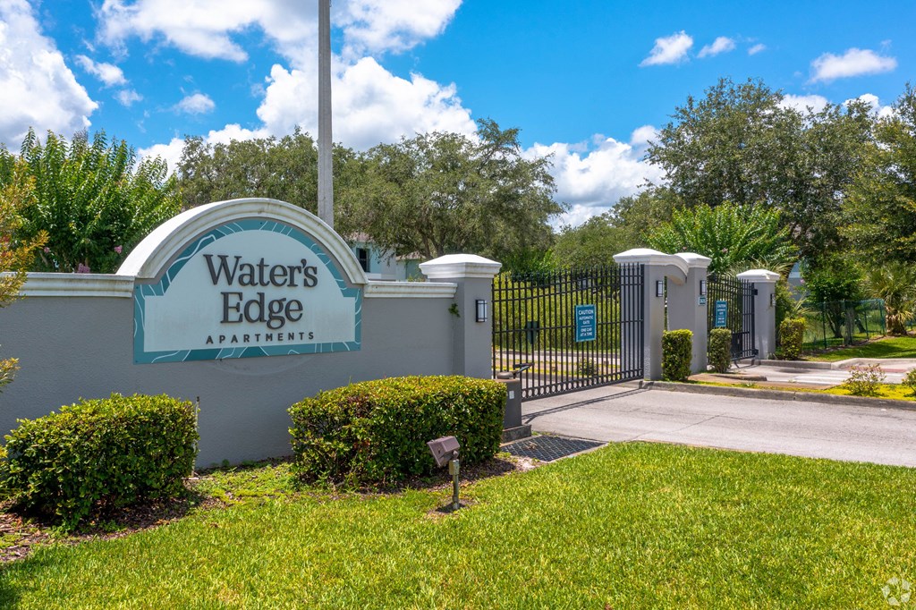 the entrance to waters edge apartments with a blue gate and green grass the entrance to waters edge apartments with a blue gate and green grass at Waters Edge Apartments, Florida