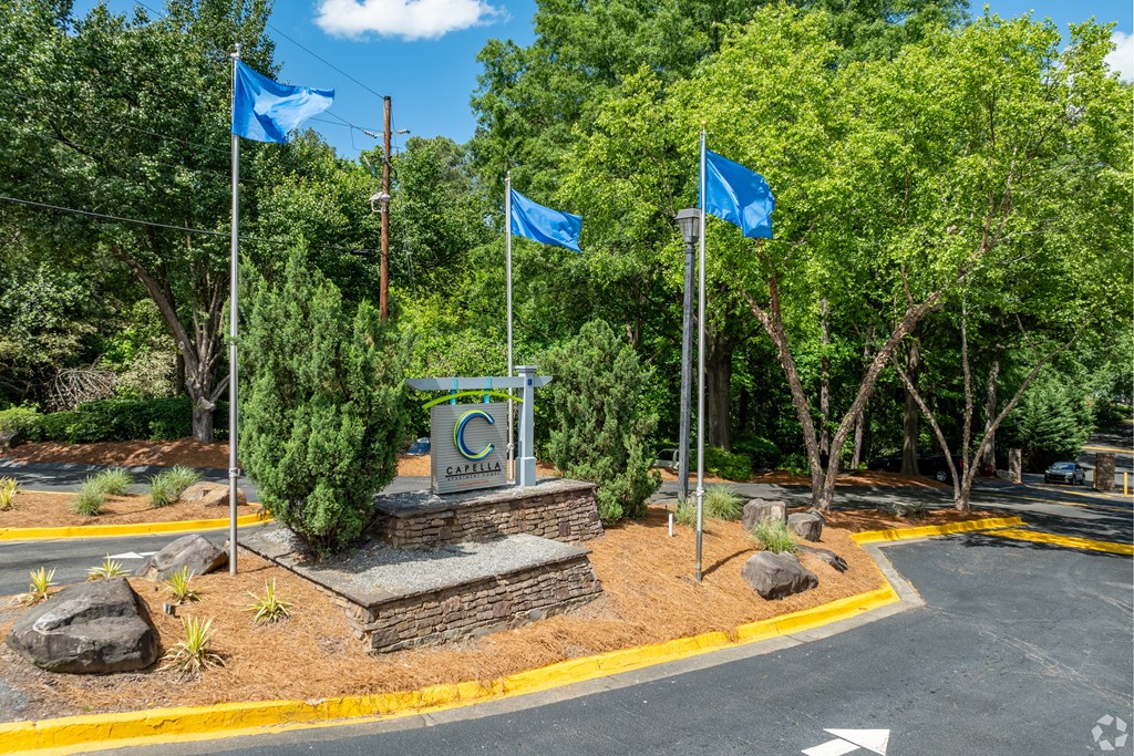 a monument with three blue flags and a road and trees