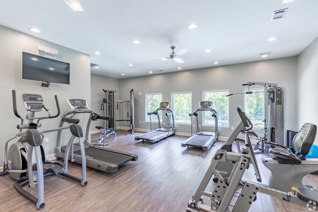 a gym with cardio equipment and a tv
