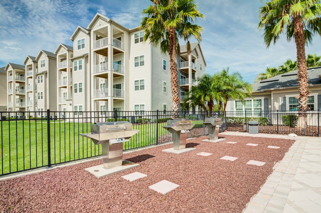 a patio with three bbq pits and two palm trees in front of an apartment building  at Century Avenues, Florida, 33813