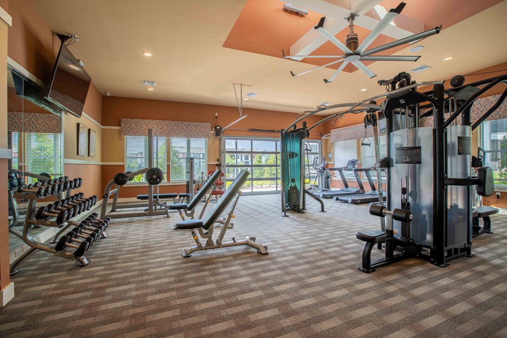 a gym with weights and other equipment in a room with windows at Century Dunes Apartments, Deland, FL