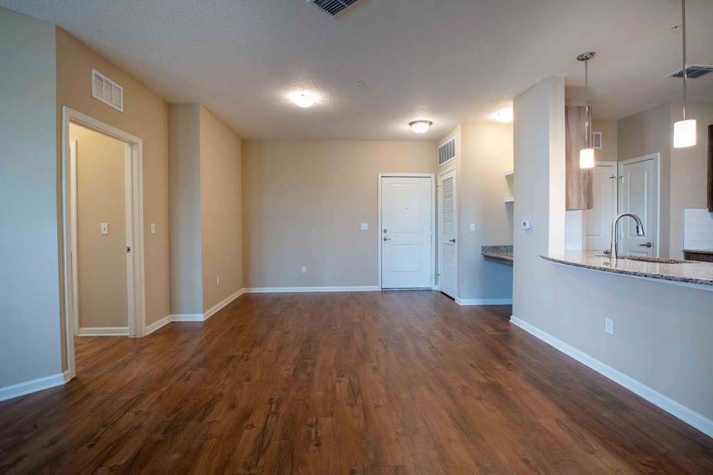 an empty living room with wood flooring and a kitchen at Century Dunes Apartments, Florida