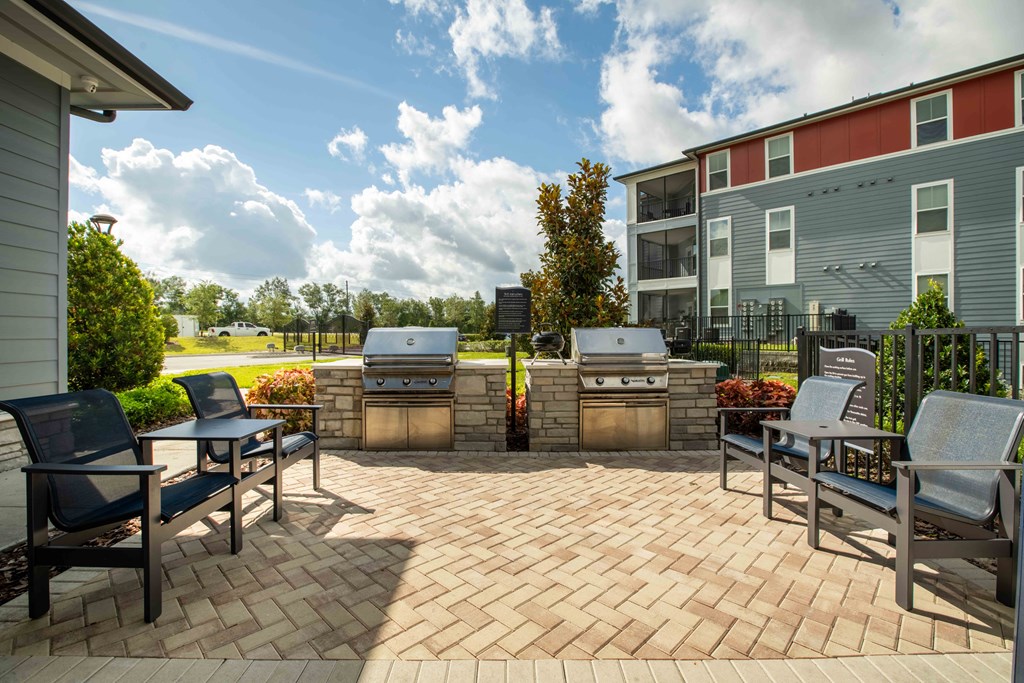 a patio with two barbecue grills and chairs on it at Century Dunes Apartments, Deland, FL, 32724