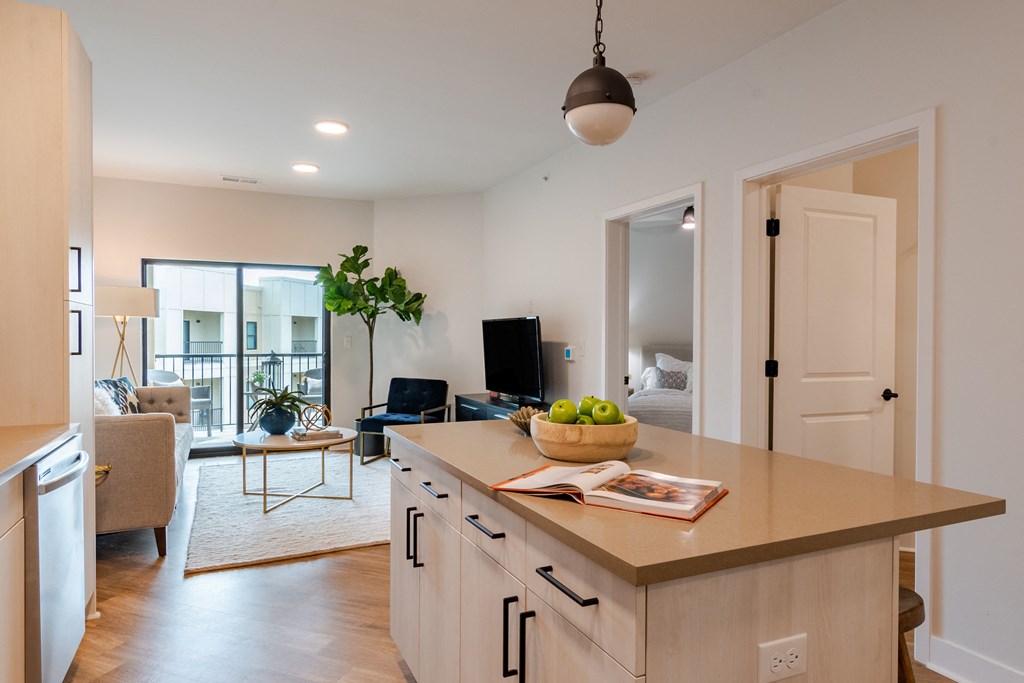 a kitchen island with a bowl of fruit on it and a living room in the background  at Century West Pryor, Lee's Summit, MO
