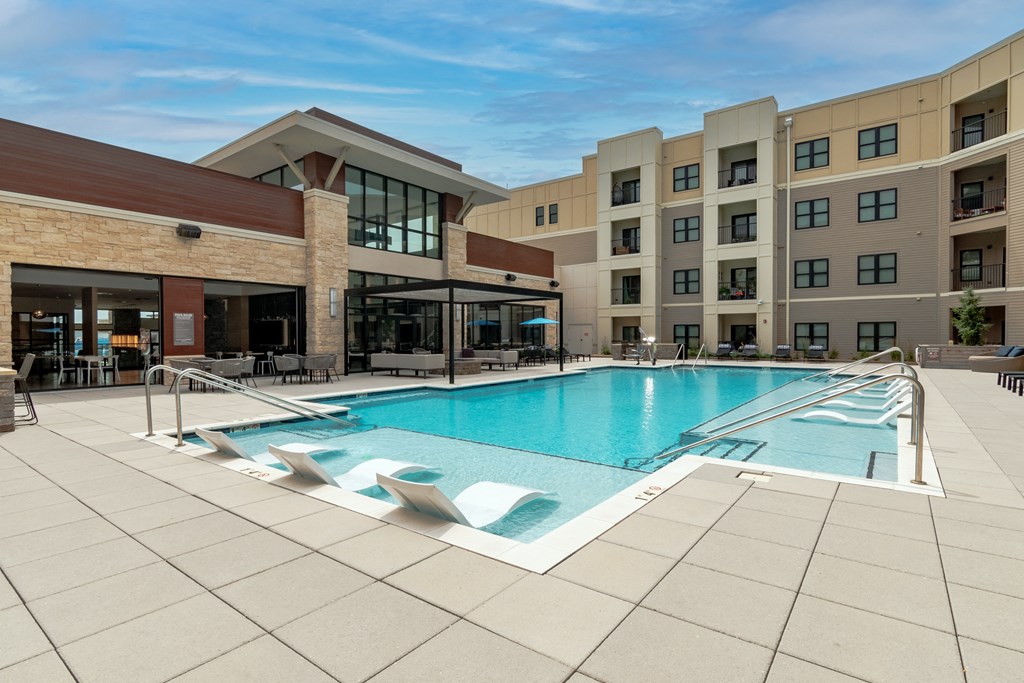 a swimming pool with lounge chairs and a building in the background  at Century West Pryor, Lee's Summit, Missouri