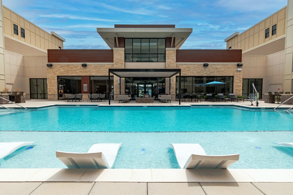 a swimming pool with lounge chairs and umbrellas in front of a building  at Century West Pryor, Lee's Summit, MO