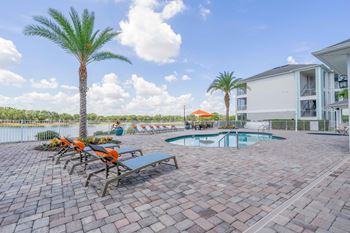 a swimming pool with chairs and palm trees next to a house