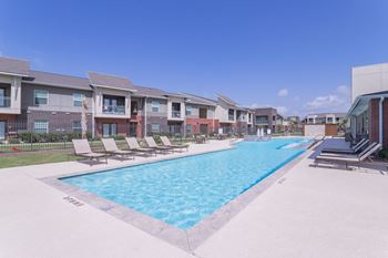 a swimming pool with lounge chairs and apartments in the background at Century Palm Bluff, Portland, Texas