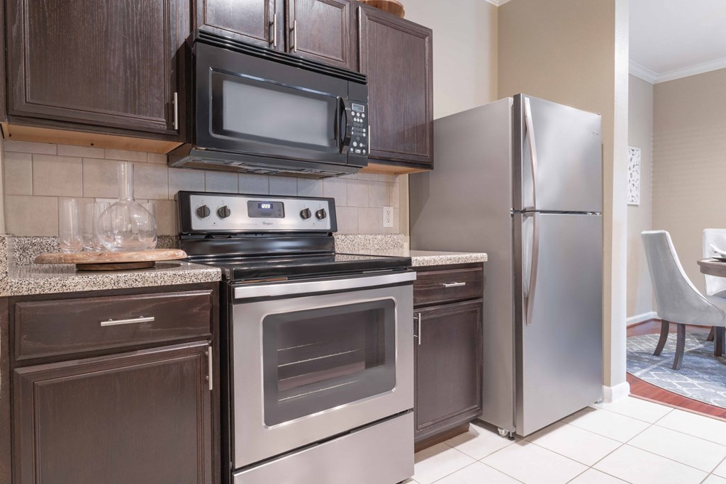 a kitchen with dark cabinets and stainless steel appliances at Century South Shore, League City