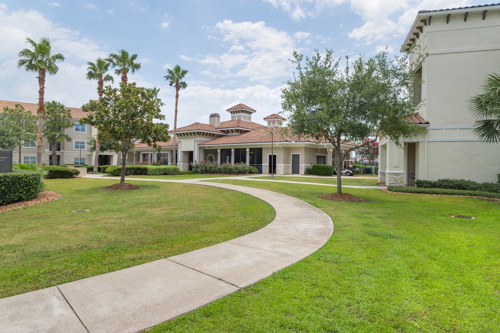 a walkway through a grassy area with trees and buildings in the background at Century South Shore, Texas